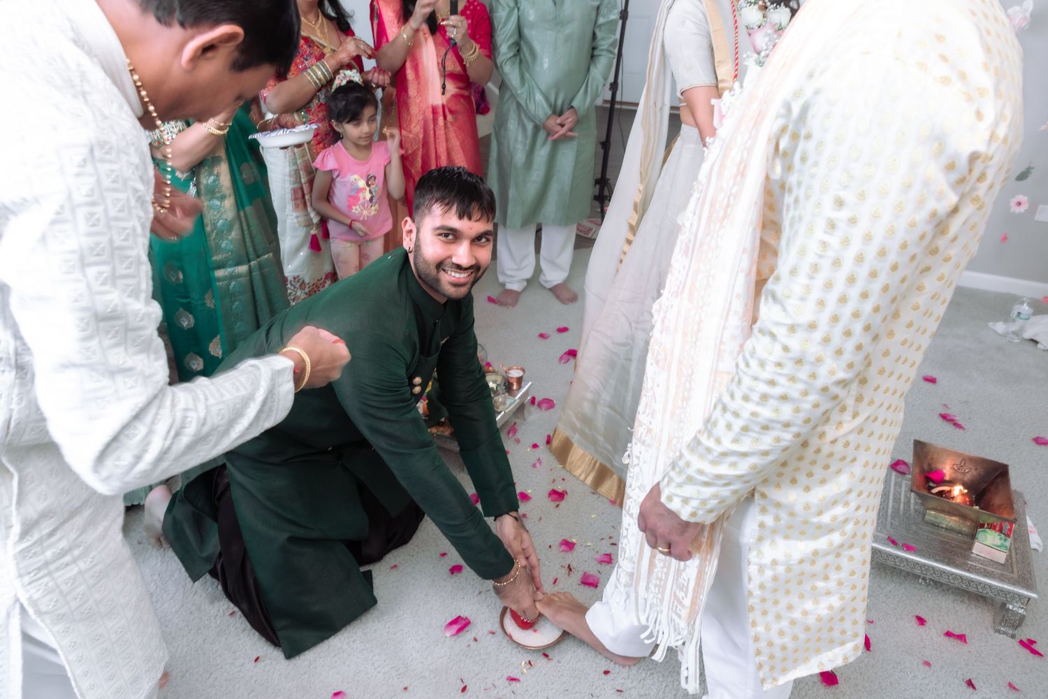 Man in green sherwani performs traditional Indian wedding ritual at groom's feet during ceremony.