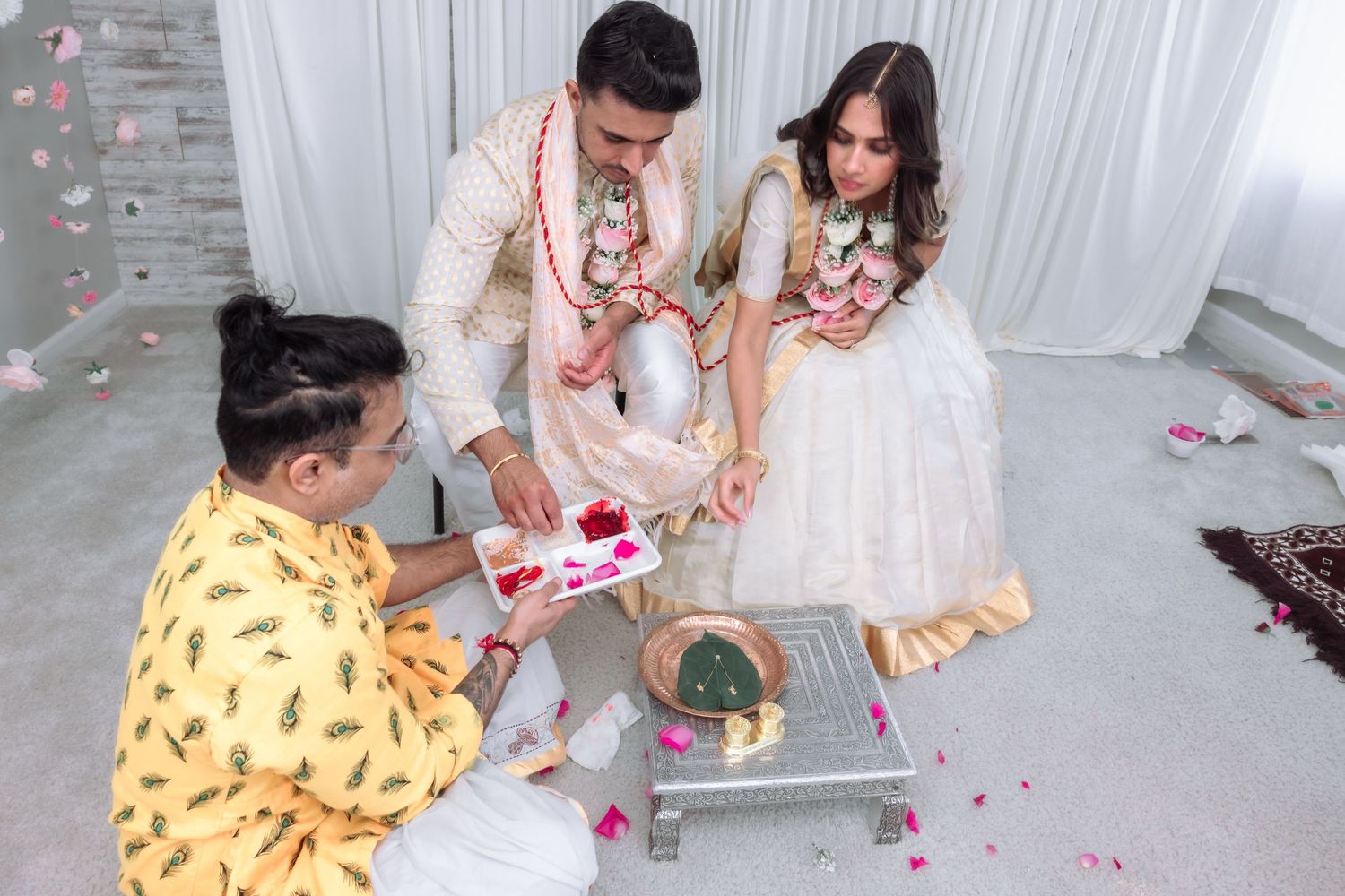 Hindu wedding ritual with priest presenting offerings to bride and groom.
