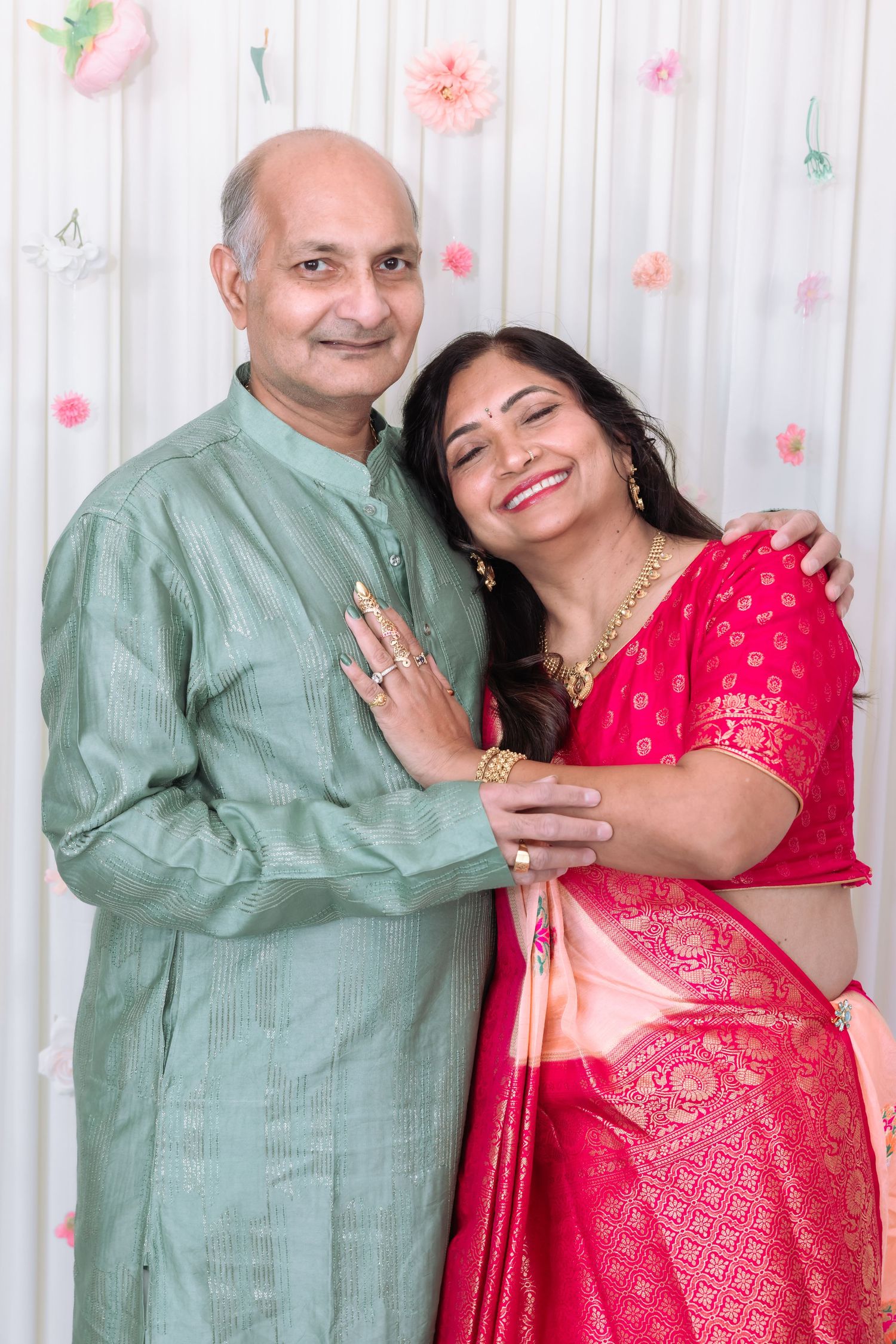Smiling Indian couple in traditional attire, man in sage kurta and woman in red saree, pose together.
