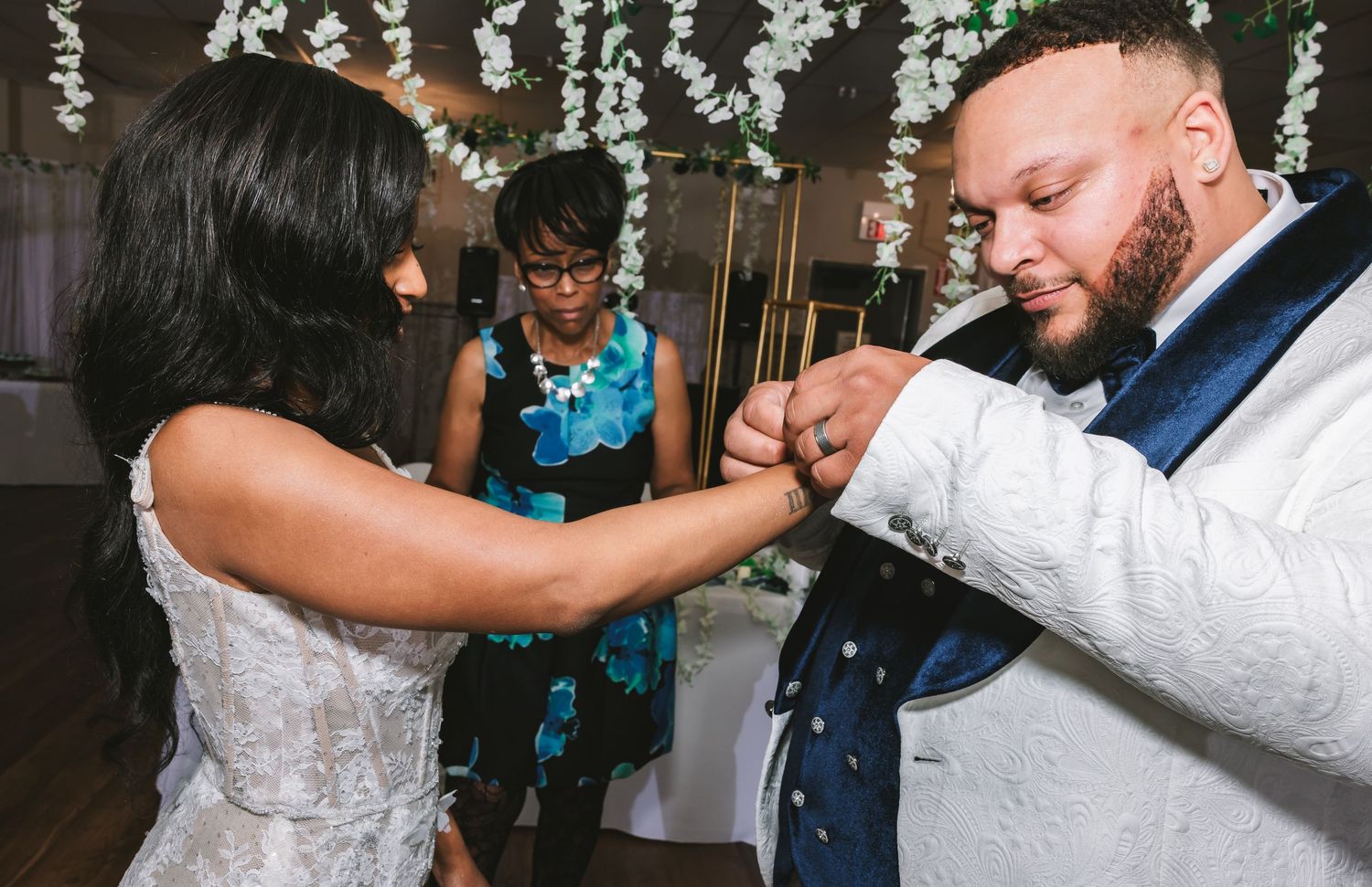 Bride placing wedding ring on grooms finger during intimate ring exchange ceremony with officiant watching closely.