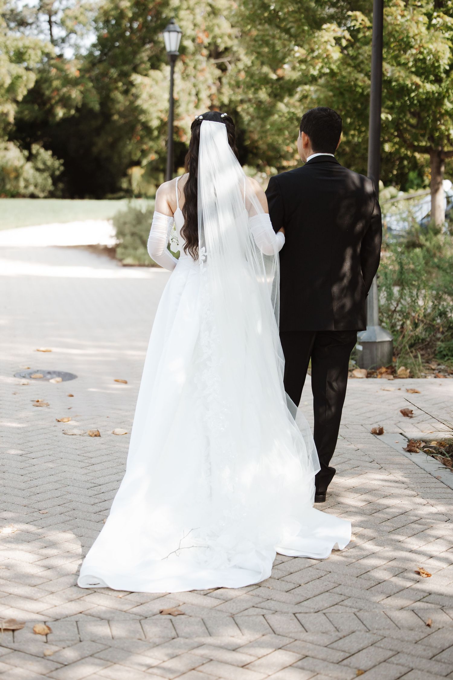 Bride and groom walking hand in hand down a brick path in a lush garden after their wedding ceremony.