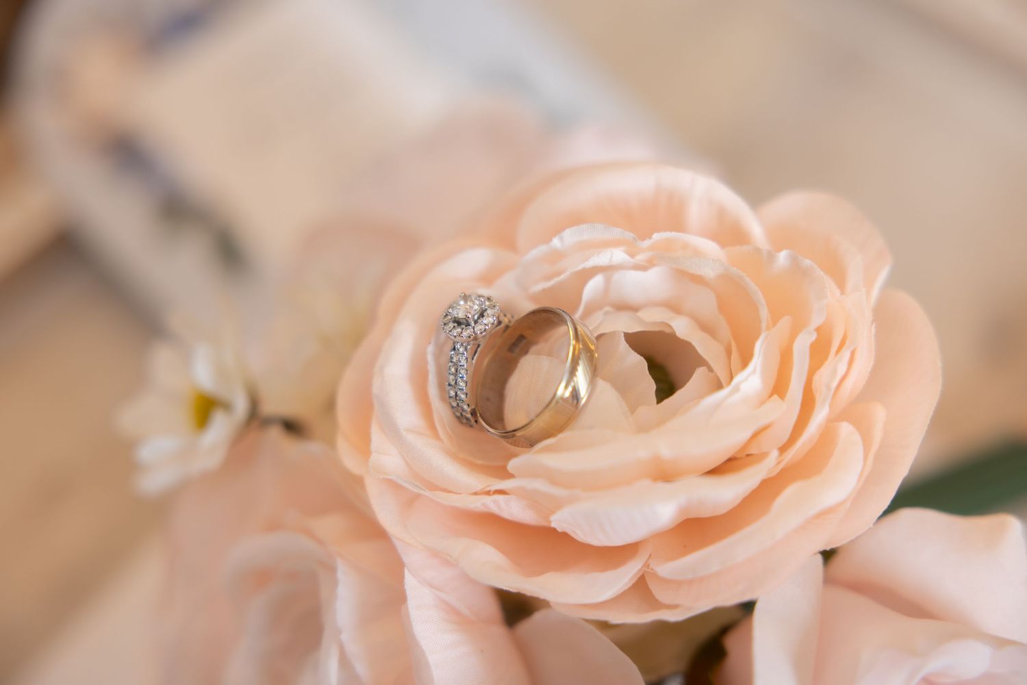 Diamond engagement ring and gold band displayed in a soft pink ranunculus bloom.