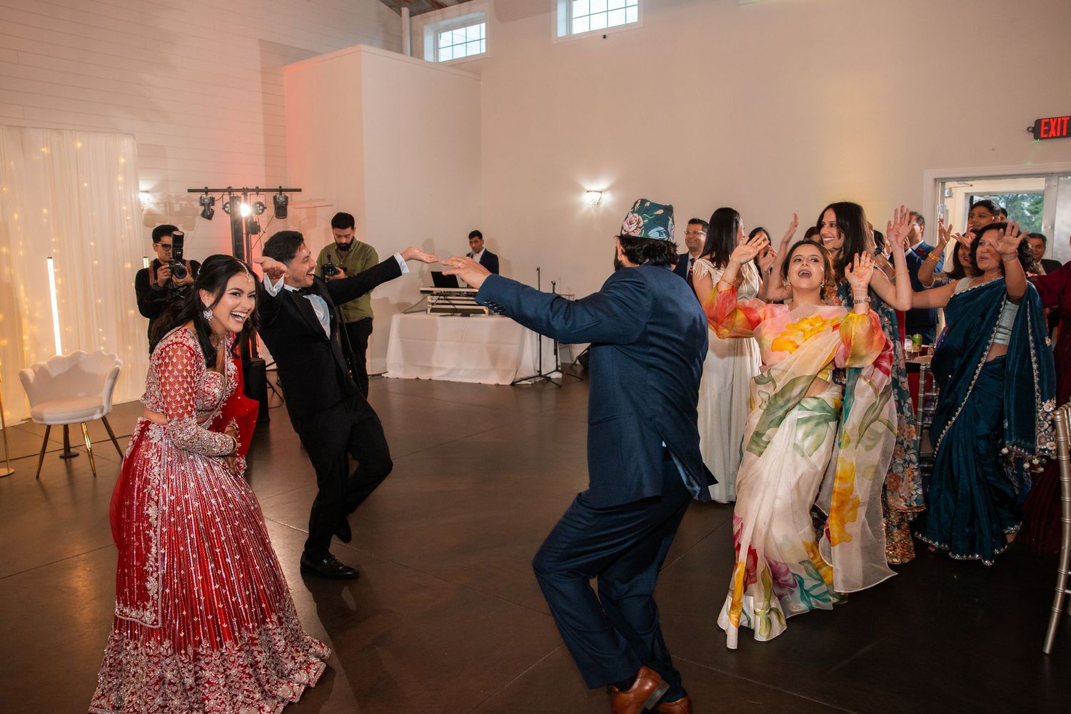 Guests dance joyfully with bride in red lehenga at vibrant Indian wedding reception.