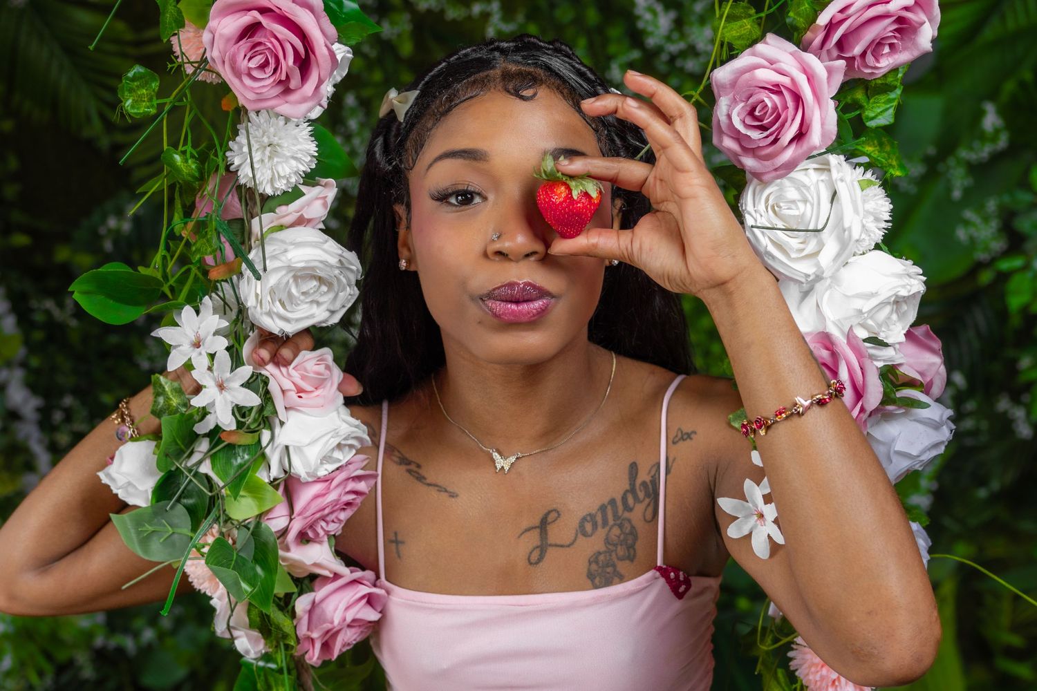Young Black woman holds strawberry near face surrounded by pink and white roses on floral swing.
