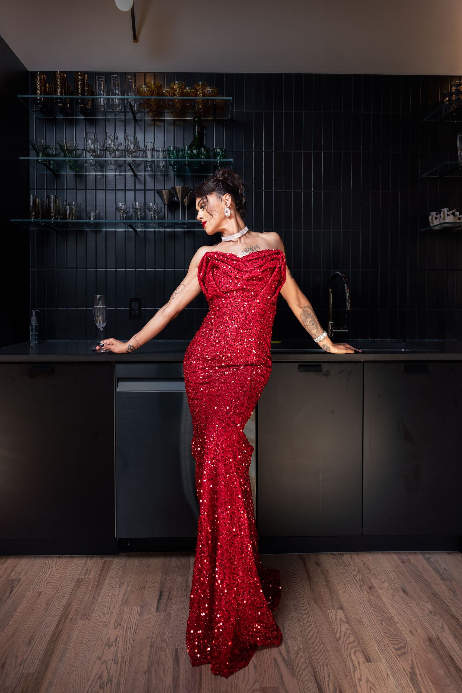 Woman in stunning red sequin mermaid gown standing in dark modern kitchen interior.