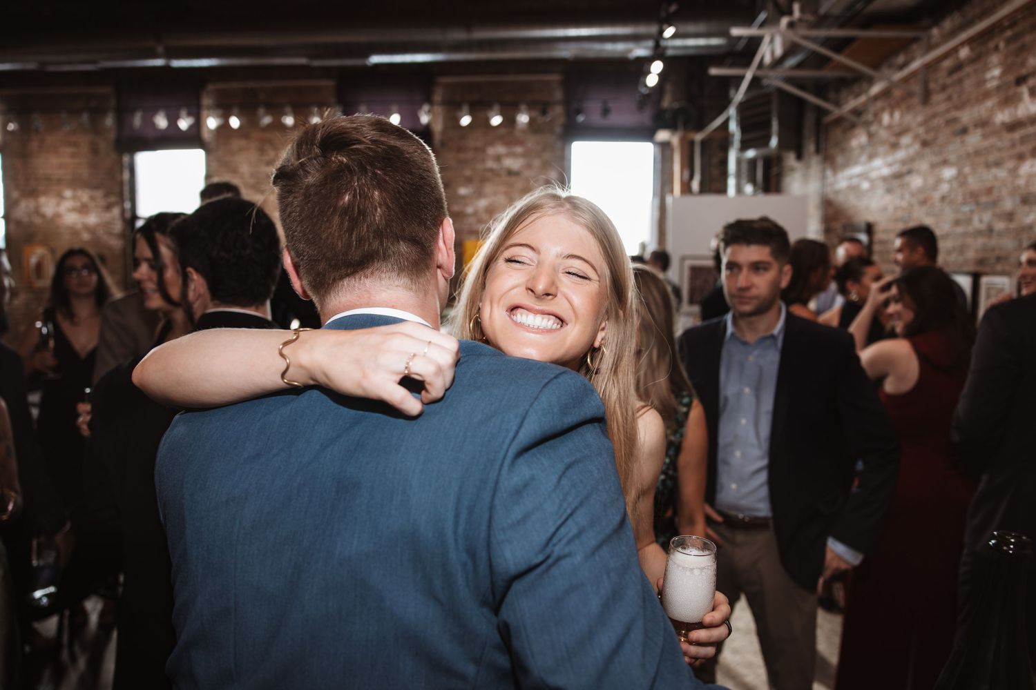 Smiling woman hugs a man in a blue suit at a lively indoor social gathering.