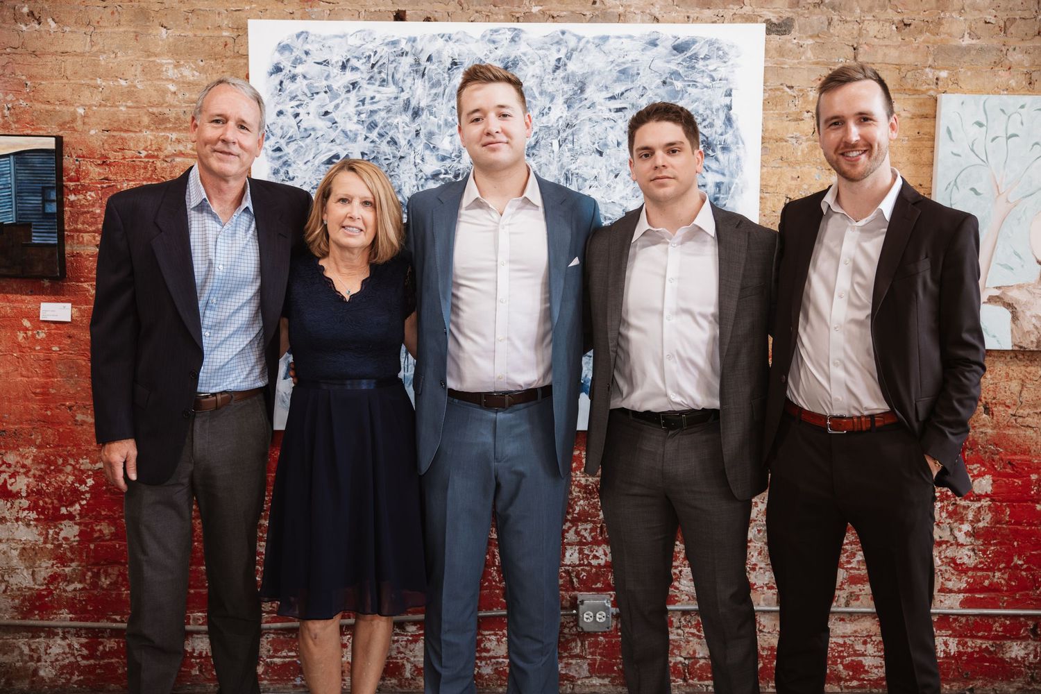 Five professionally dressed guests pose together smiling at an elegant art gallery reception event.