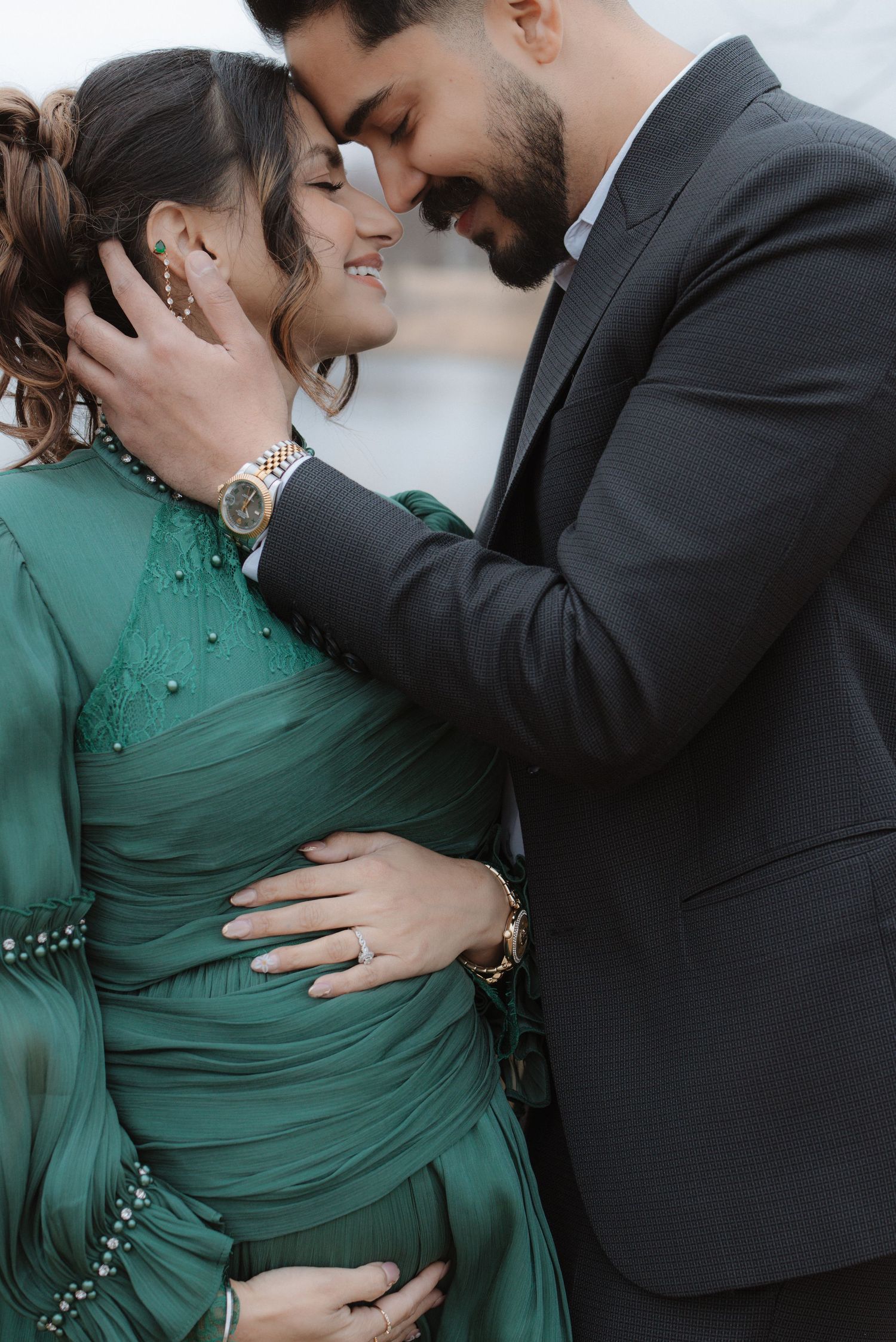 Close-up of expecting couple sharing intimate forehead touch, woman in green gown near lake.