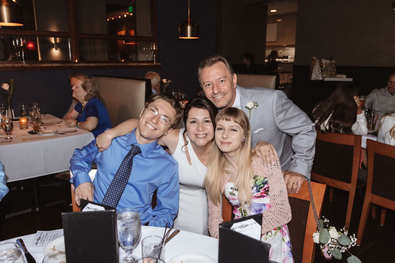 Happy family of four posing together at a wedding reception dinner table in a restaurant venue.