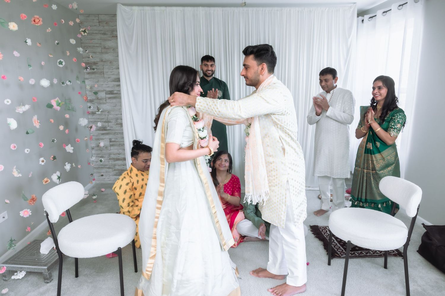 Bride and groom smile while exchanging garlands during a traditional Indian wedding ceremony indoors.