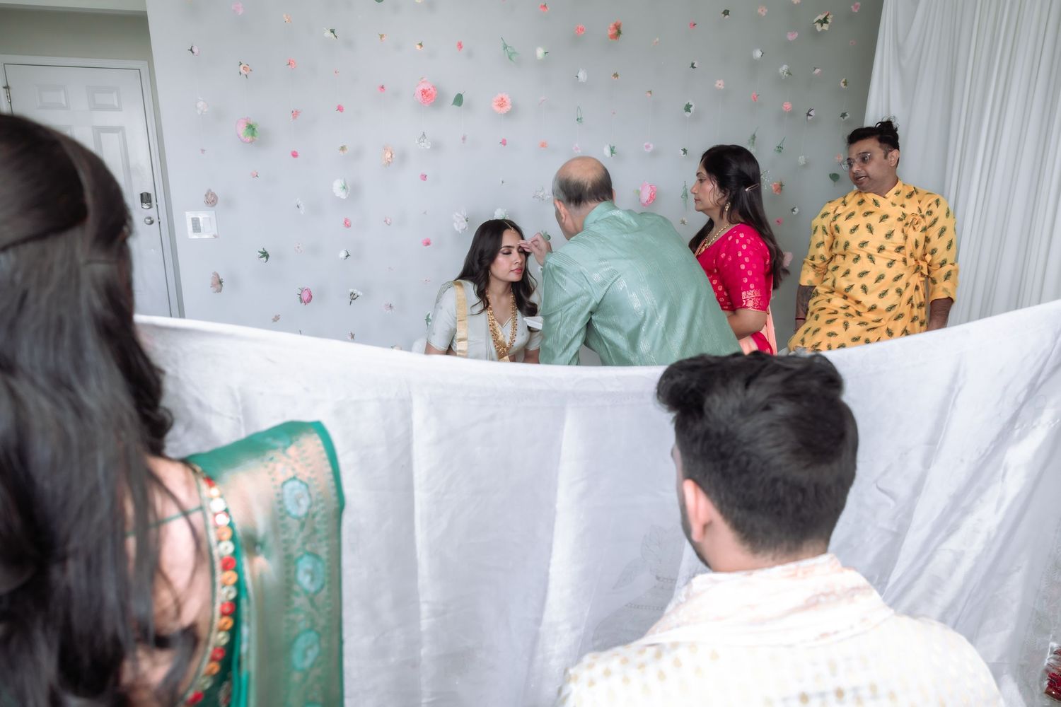 Family members hold a white cloth as a partition during a traditional Indian wedding ceremony indoors.