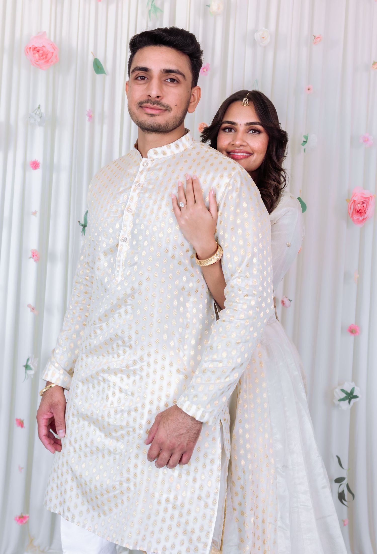 Indian couple in white traditional outfits pose back-to-front at a festive celebration.