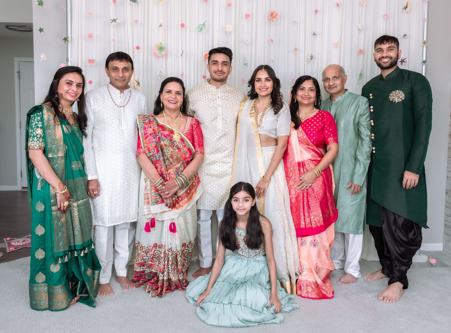 Indian wedding family portrait with nine members in vibrant traditional ethnic attire at celebration venue.