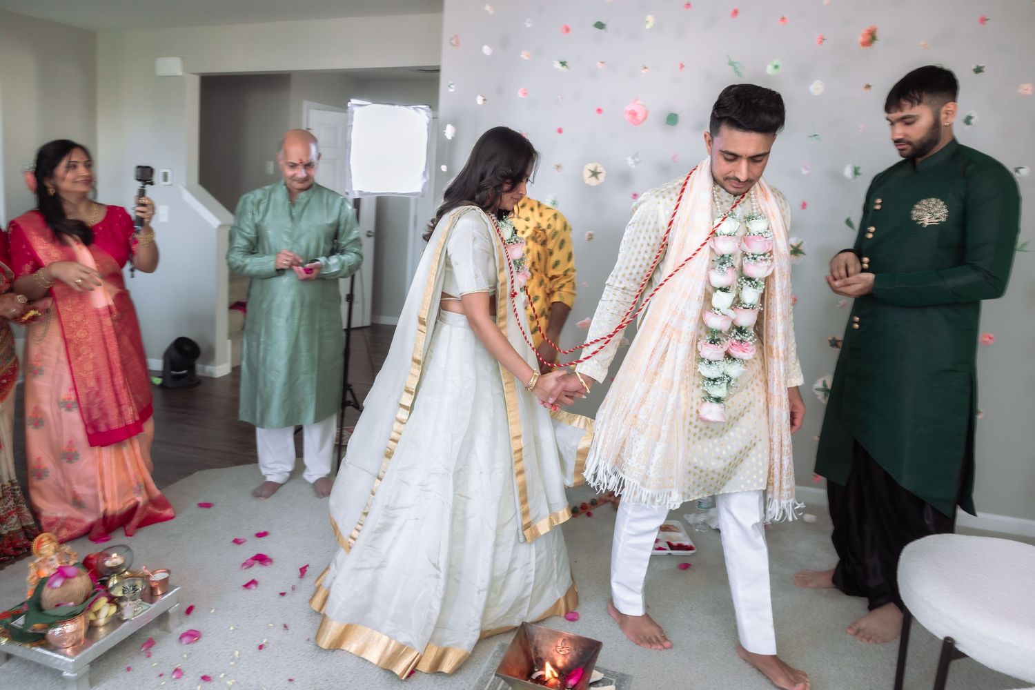Indian bride and groom participate in traditional stepping ritual during indoor Hindu wedding ceremony.