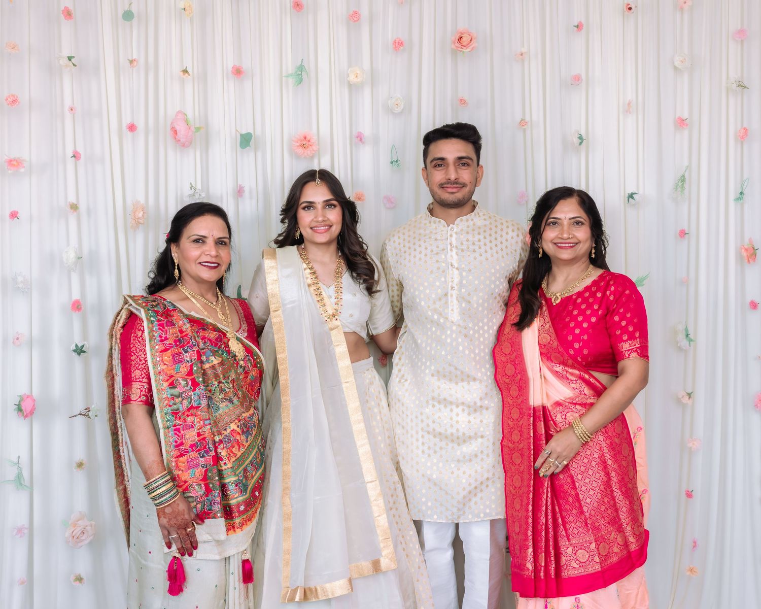 Indian family of four posing in traditional wedding attire with bride and groom in white.