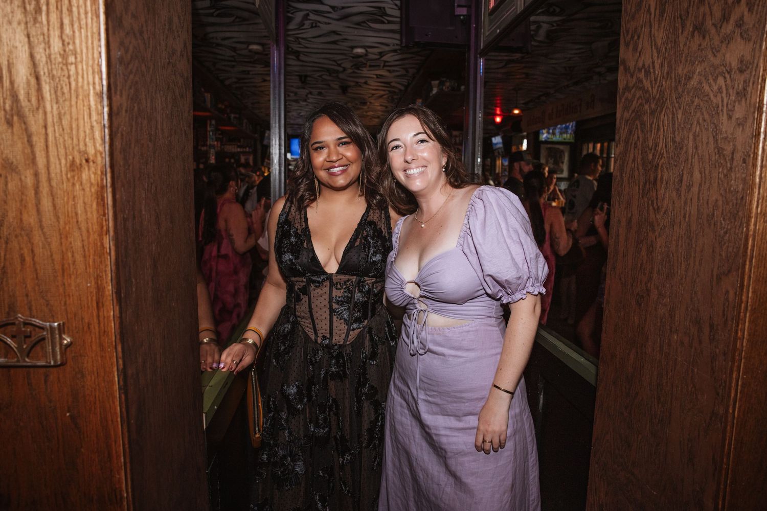 Two women posing together in elegant dresses at a dimly lit venue.