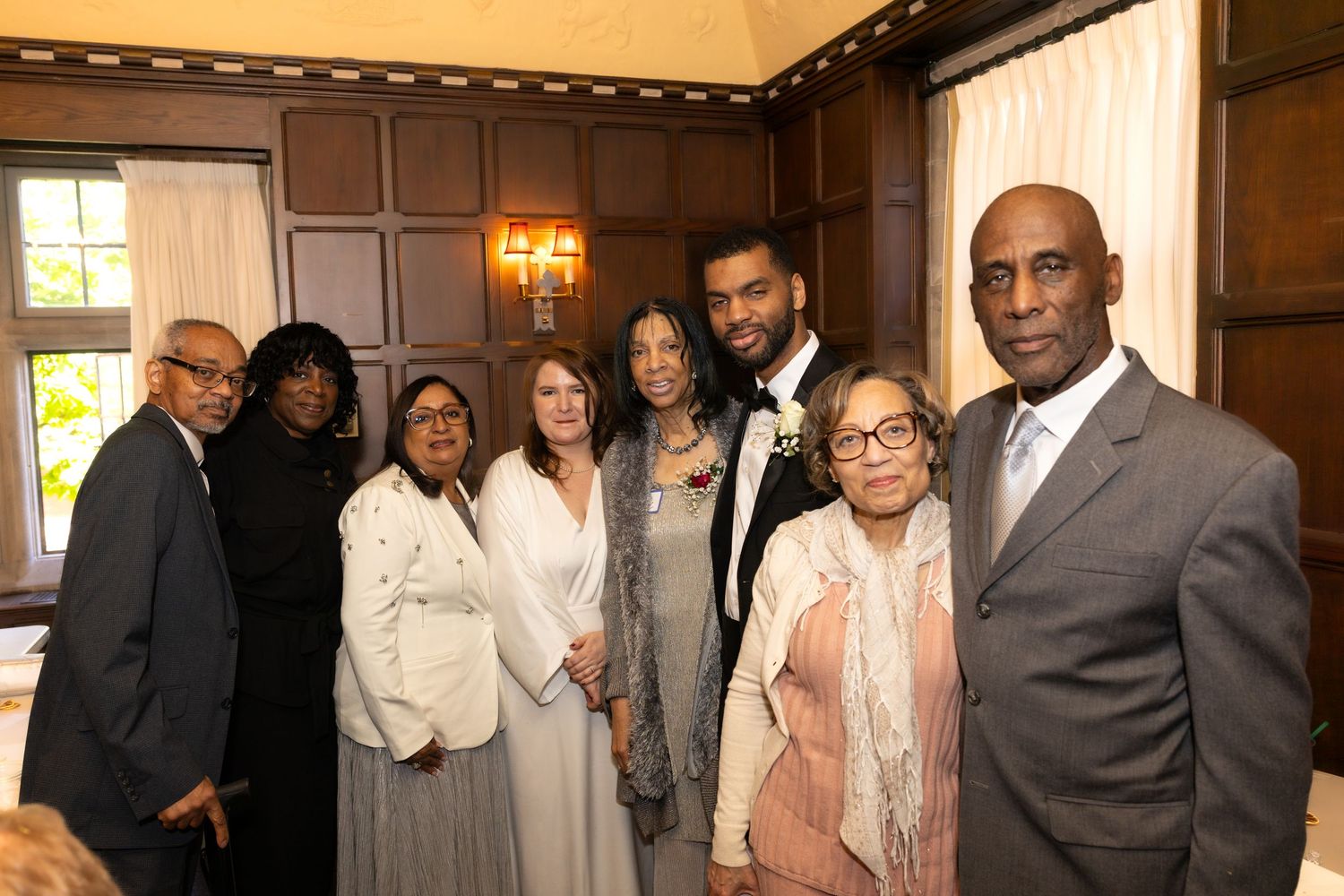 Group of eight people posing together smiling at an elegant indoor wedding reception.