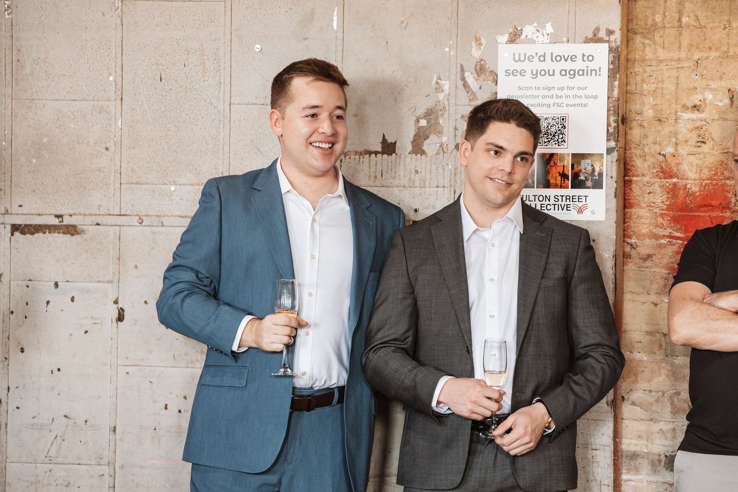 Two smiling men in suits holding champagne glasses at a corporate or social networking event.