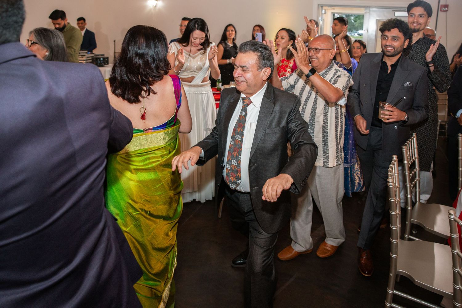 Guests in colorful attire dance together at lively Indian wedding reception celebration.