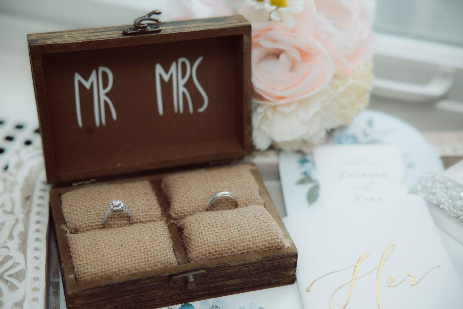 Wedding rings in a rustic wooden Mr and Mrs box beside a pink floral bouquet.