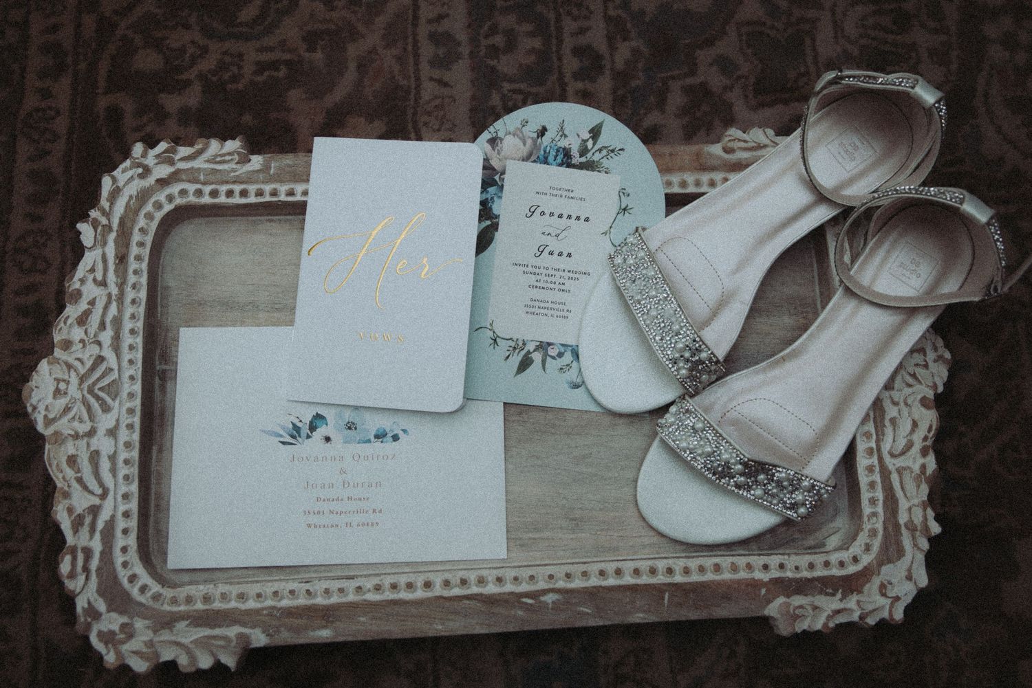 Wedding flat lay featuring floral invitation, menu card, and embellished bridal heels on tray.