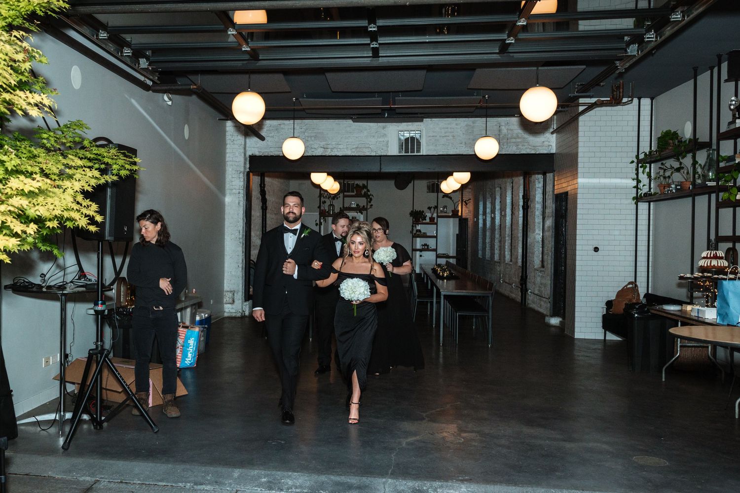 Groomsman in tuxedo escorting bridesmaid in black dress down wedding venue aisle.