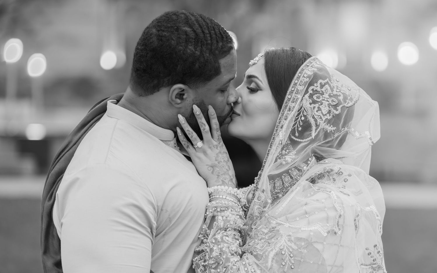 Black and white photo of interracial Muslim couple sharing romantic kiss on wedding day.