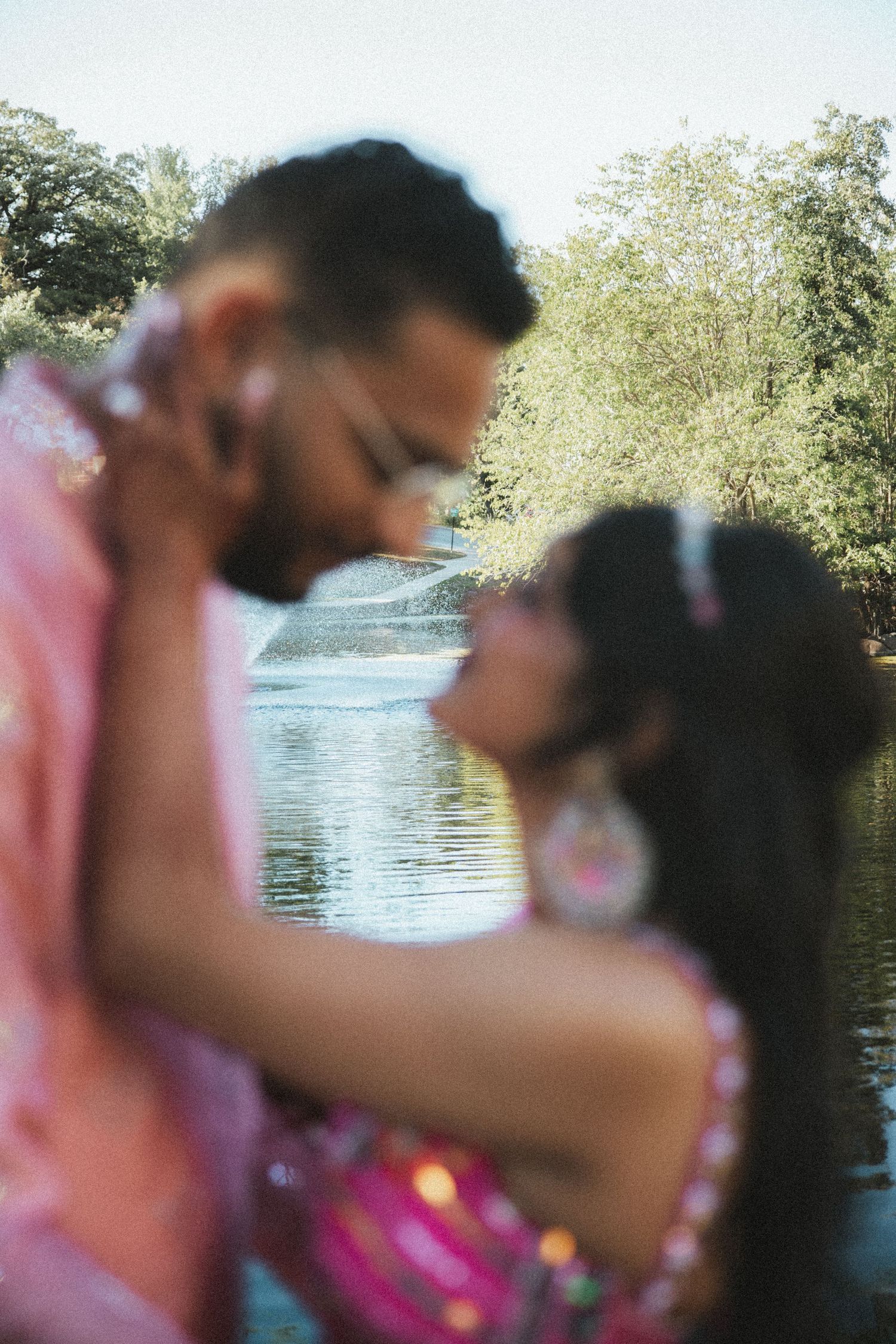 Artistic blurred portrait of Indian couple in pink traditional attire sharing an intimate moment by a lake.