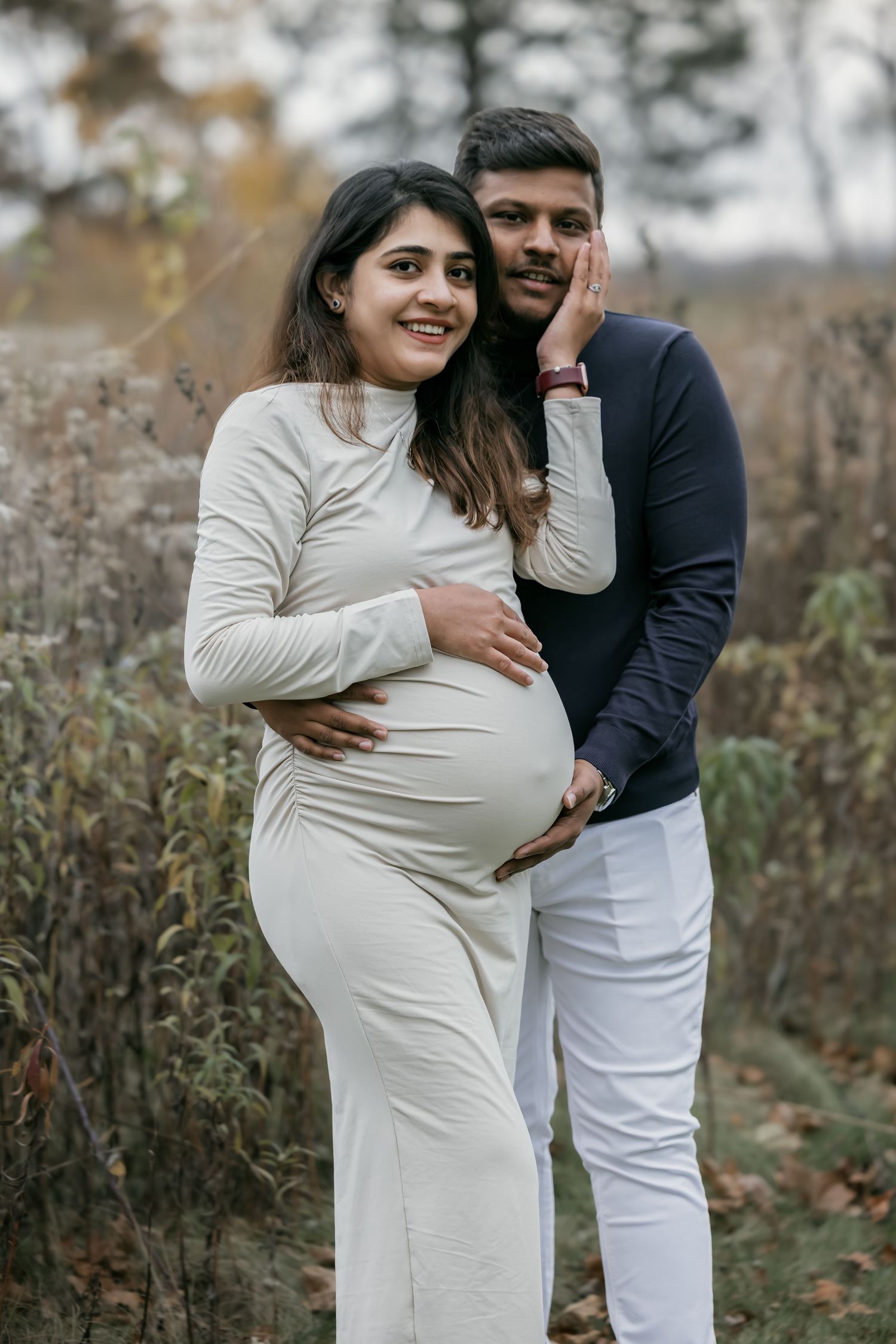 Happy pregnant couple posing together in autumn field during maternity photoshoot.