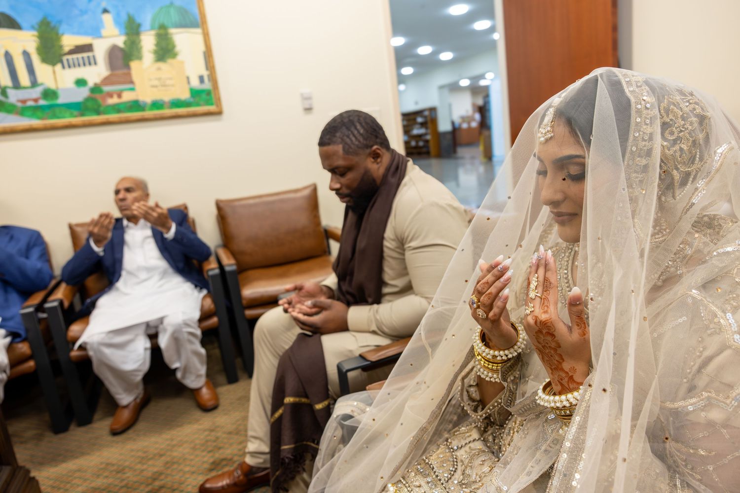 Bride and groom in prayer during Islamic nikah ceremony with elderly guest seated nearby in mosque.