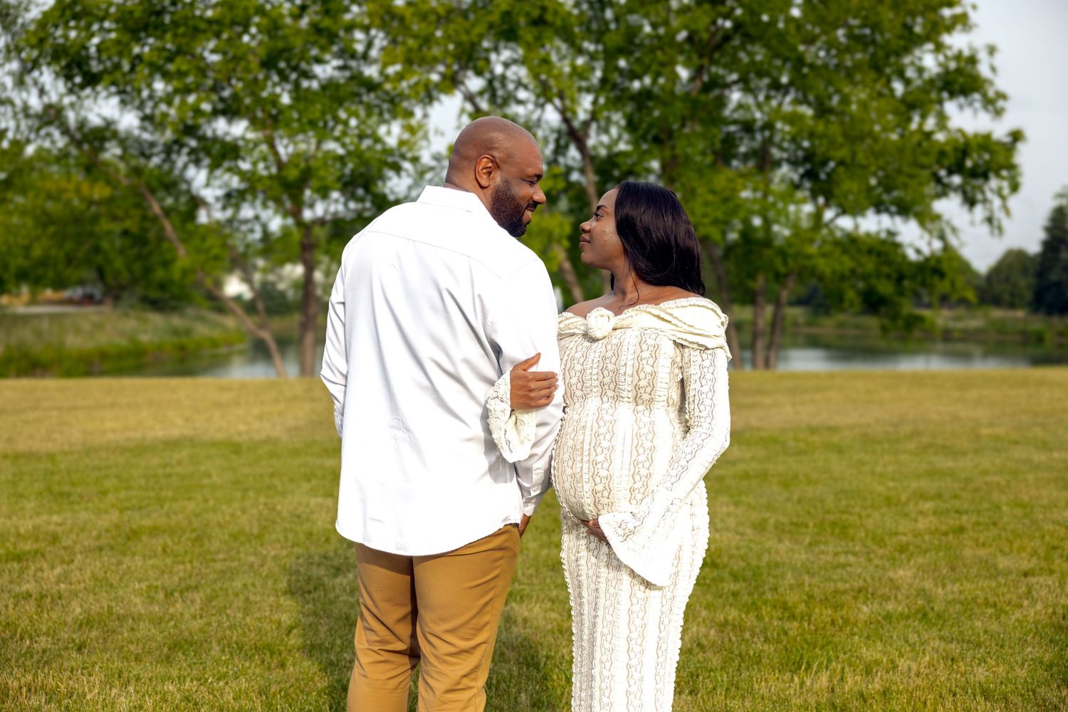 A pregnant couple walks hand in hand through a lush park.