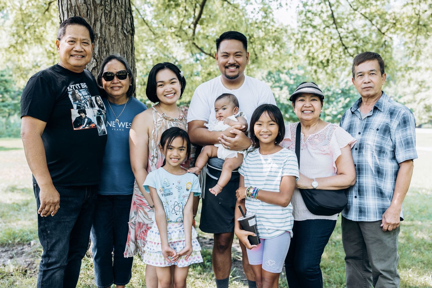 Extended Asian family group portrait outdoors under trees on a sunny day.