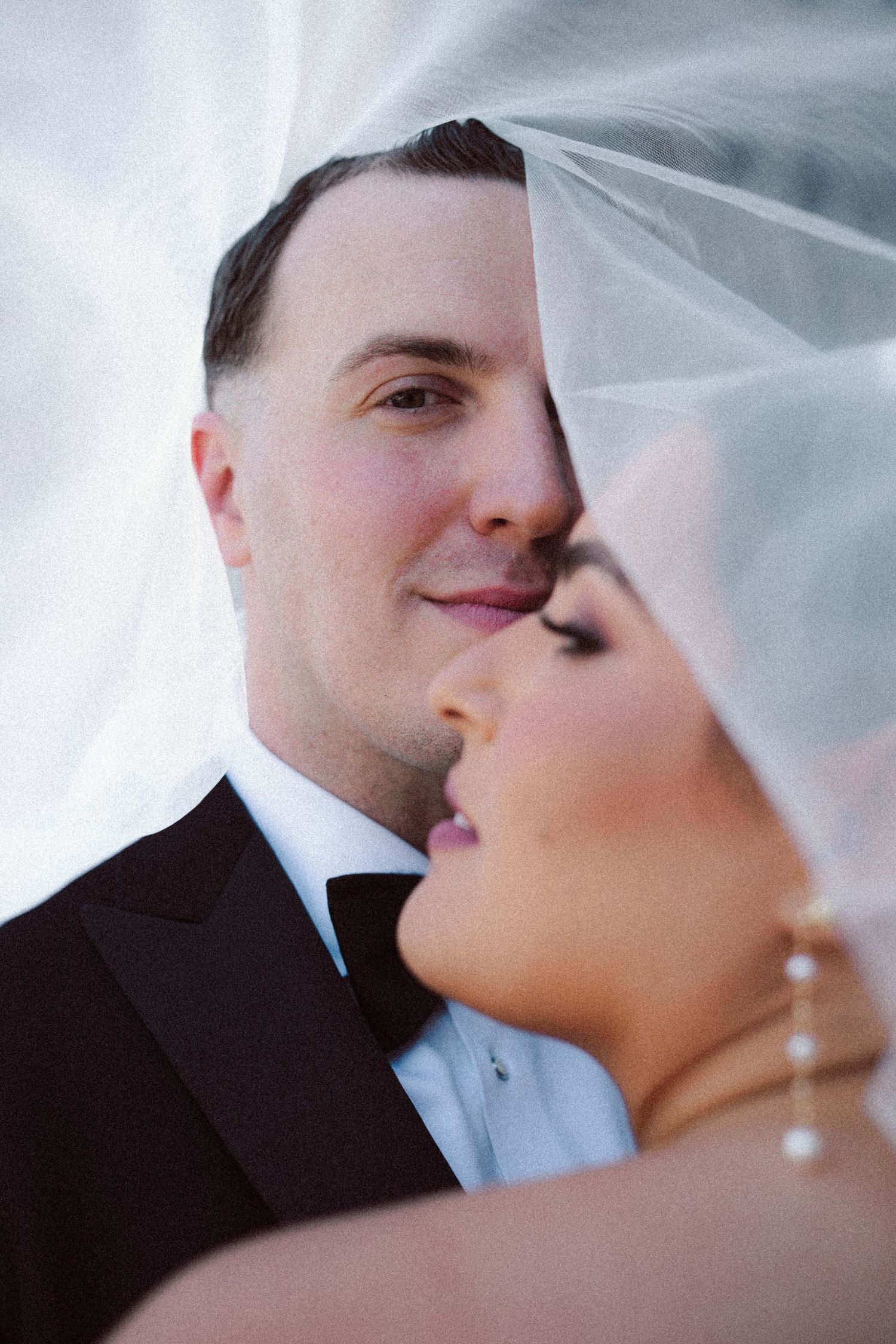 Romantic wedding portrait of bride and groom sharing an intimate moment under a flowing white veil.