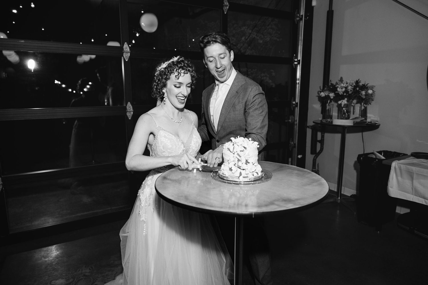 Bride and groom cutting their wedding cake together in a black and white reception photo.
