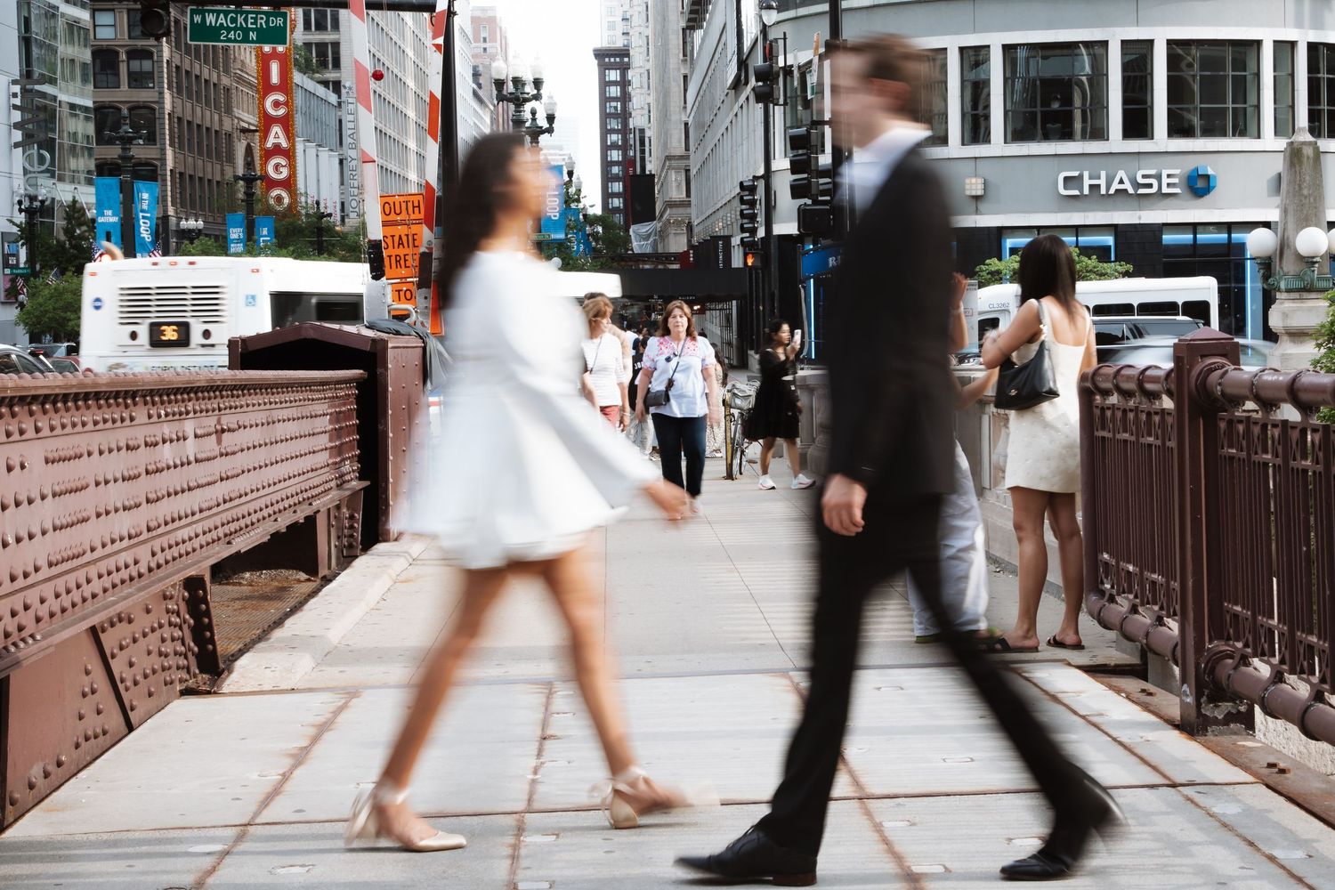 Couple in wedding attire walking on a Chicago bridge with busy city street scene.