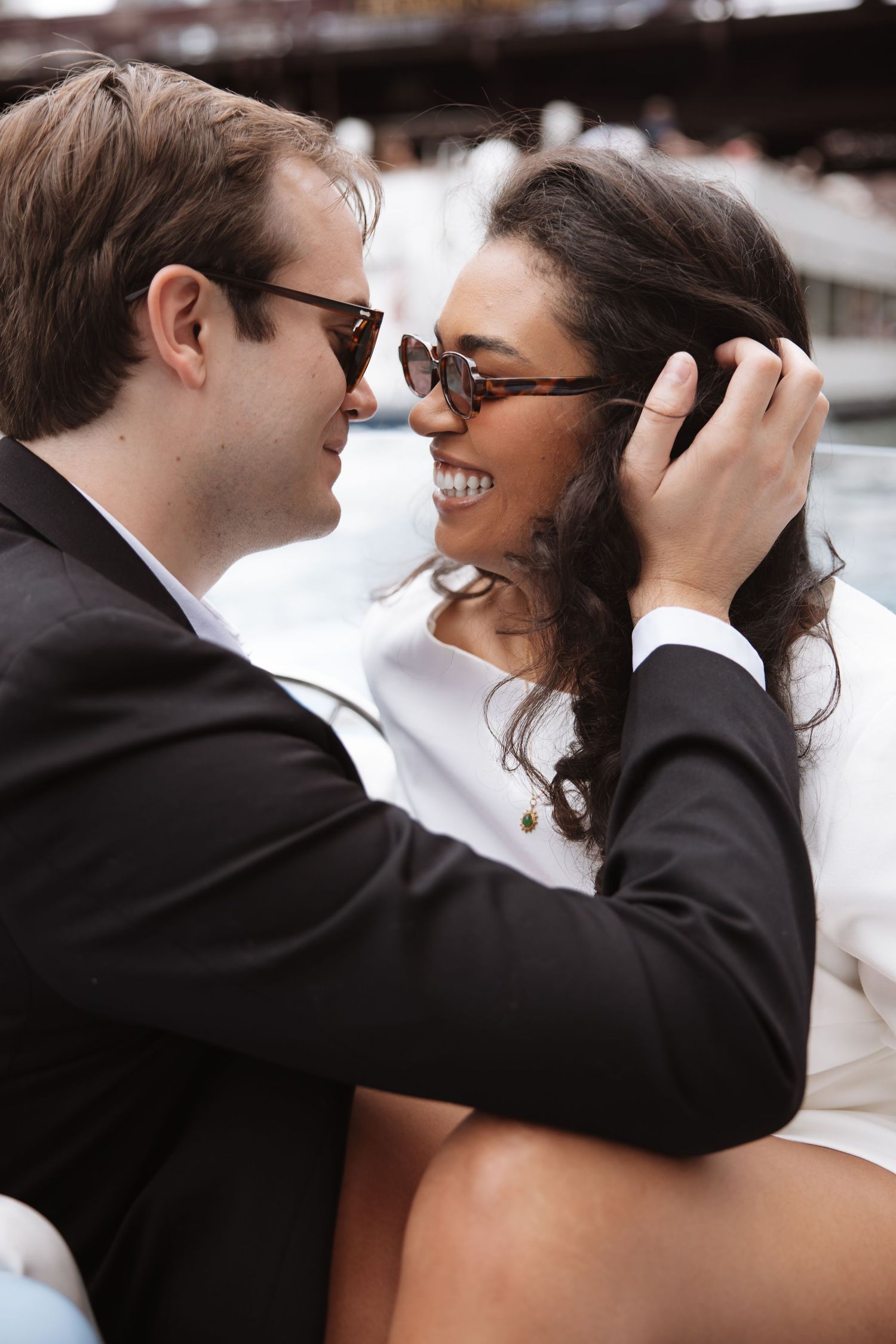 Smiling couple in sunglasses sharing a romantic moment on a boat in the city.