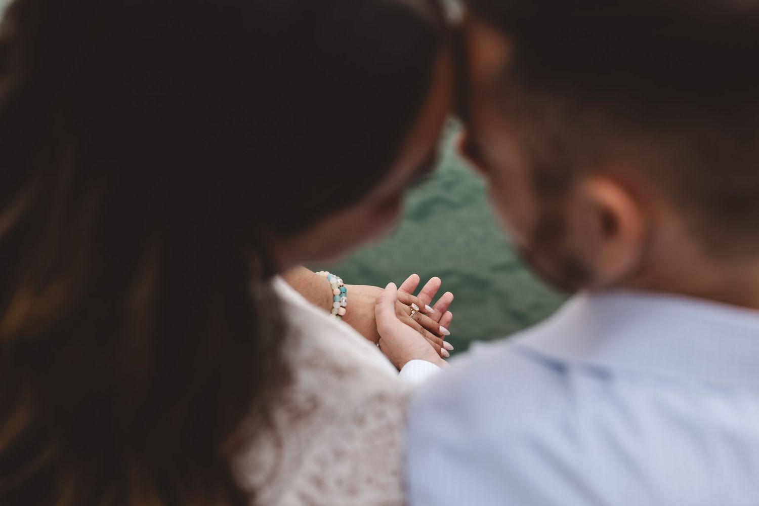 Close-up of engaged couple holding hands showing engagement ring with bokeh background.