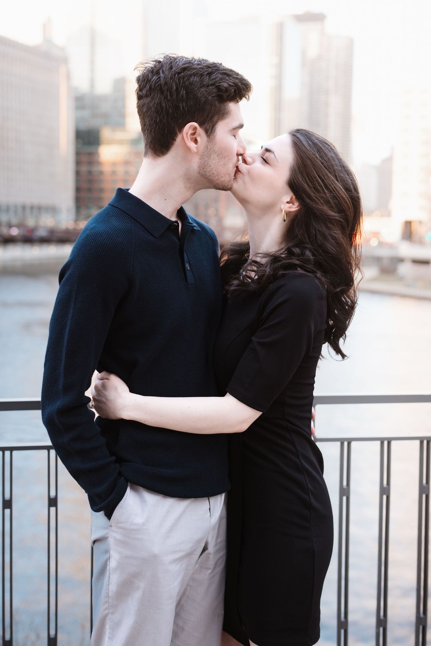 A couple shares a romantic kiss on a bridge with Chicago city skyline in the background.