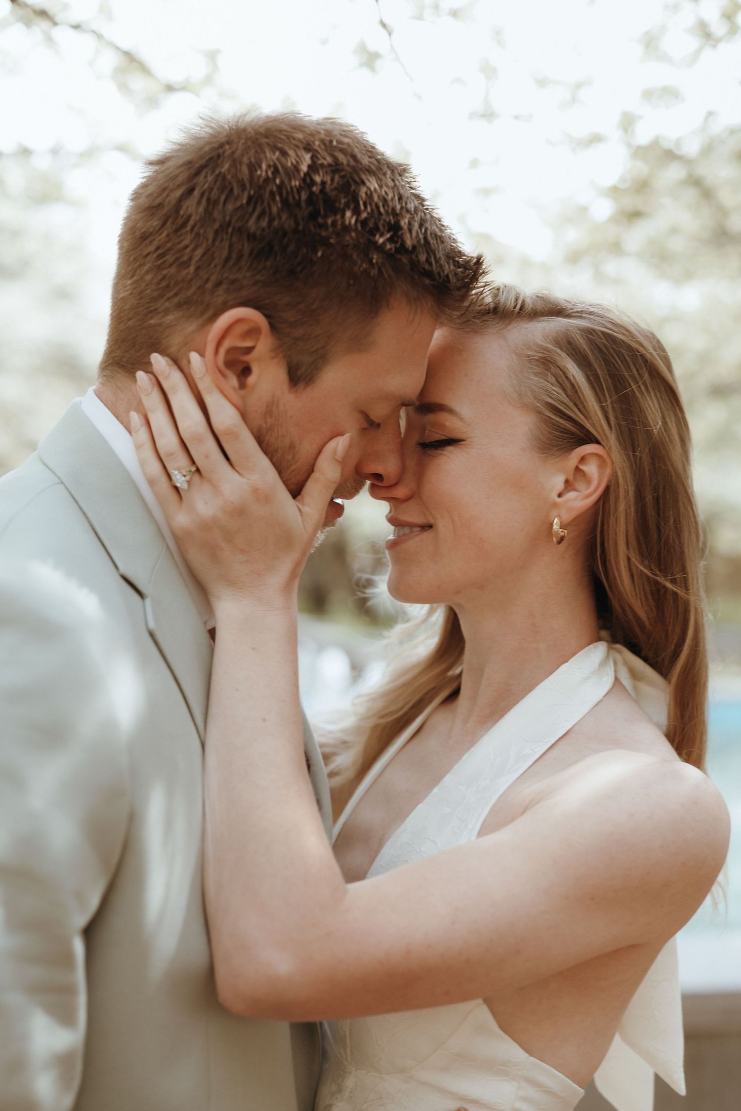Bride and groom share a tender forehead touch outdoors, bride wearing engagement ring and halter dress.