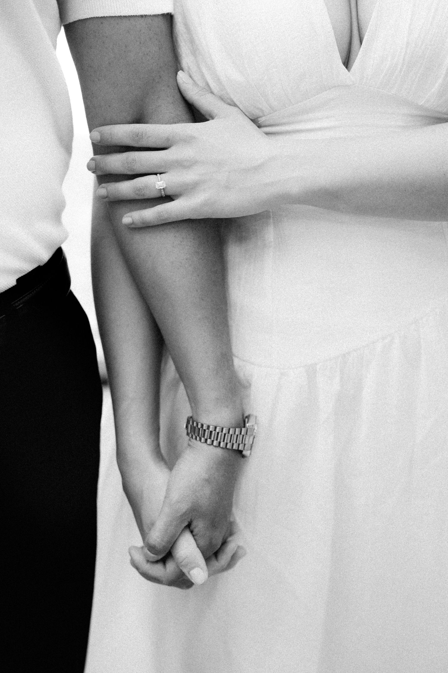 Black and white photo of a couple holding hands, bride in white dress with groom, wearing a watch and ring.