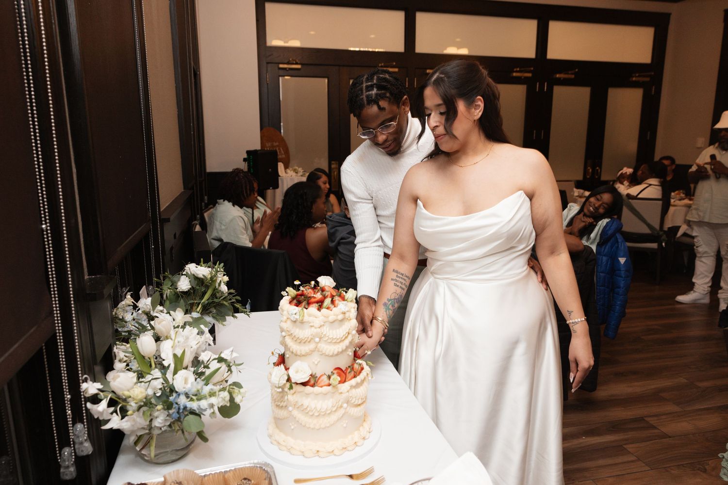 Smiling bride and groom cut their decorated wedding cake together at their reception.