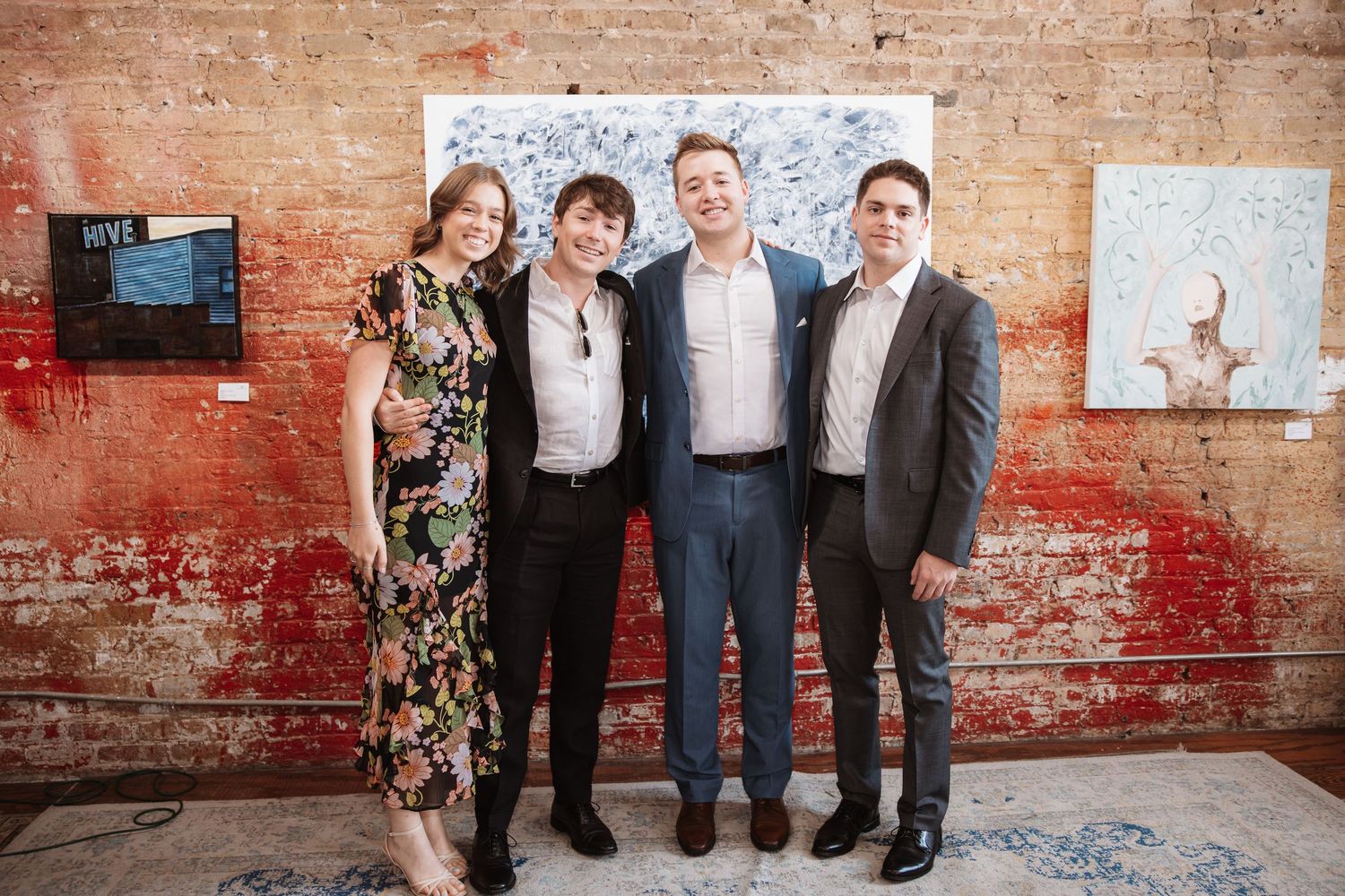 Four attendees pose happily together at a stylish art gallery event with paintings on display.