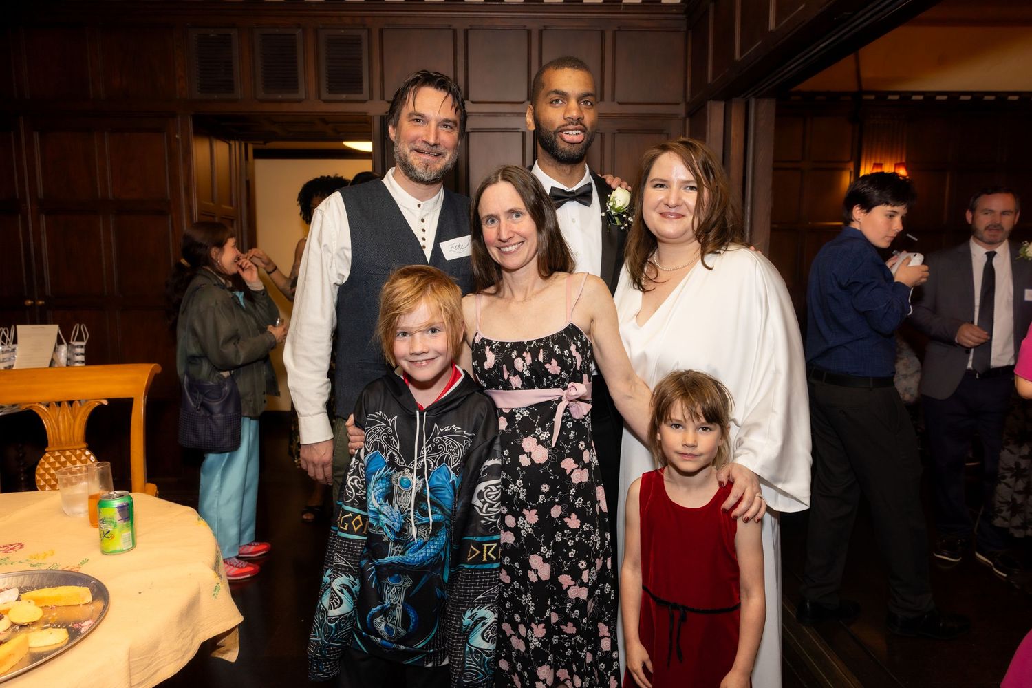 Wedding couple poses with family and children at elegant indoor reception venue.