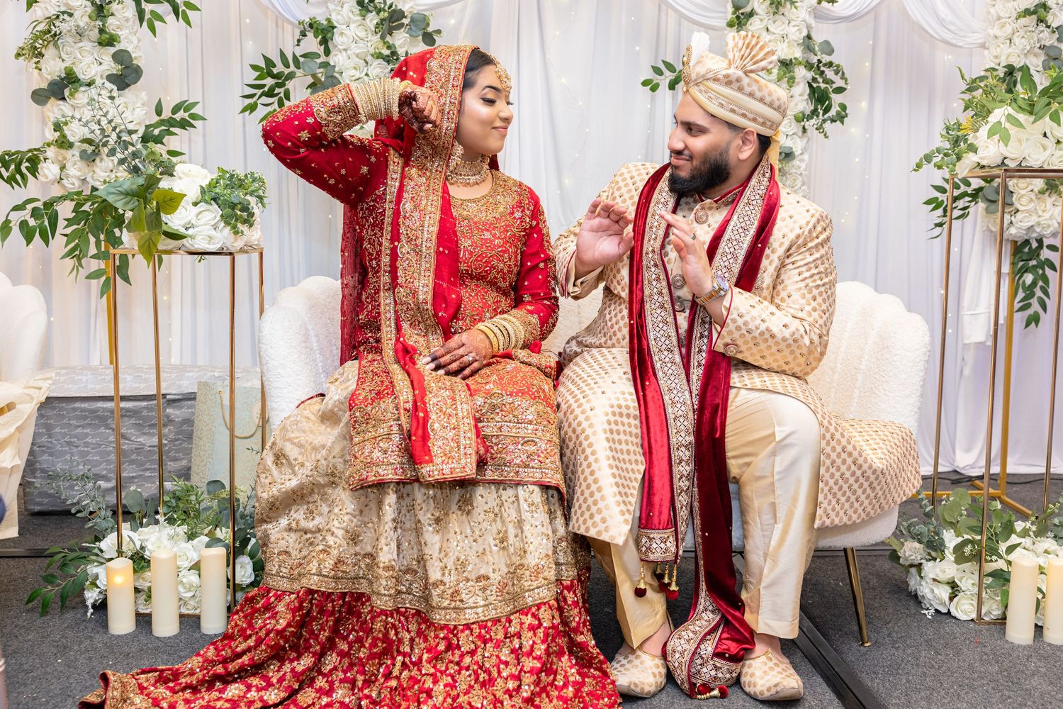 Indian bride and groom in ornate traditional red and gold wedding attire at ceremony.