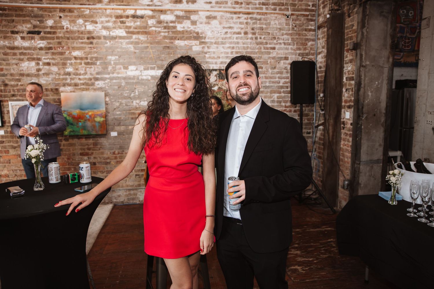 Woman in red dress and man in black suit smiling together at an art gallery event.