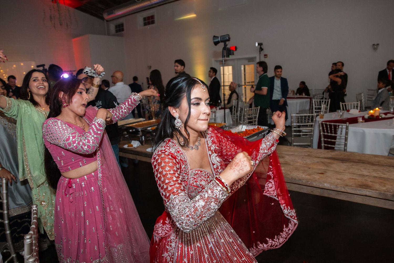 Women in traditional Indian attire performing elegant dance moves at a wedding reception celebration.