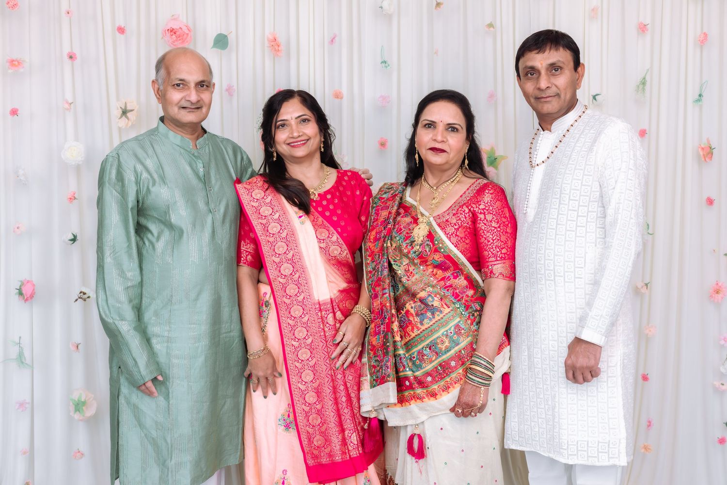 Two Indian couples posing together in colorful traditional attire at a festive celebration indoors.