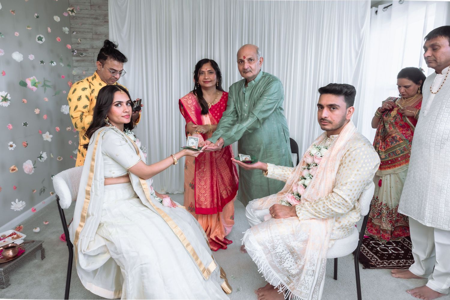 South Asian wedding ceremony with bride in white lehenga and groom in cream sherwani surrounded by family.