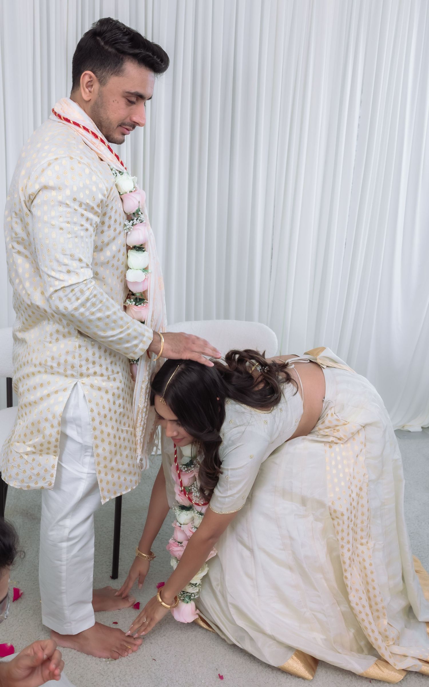 Groom gently places his hand on bride's head as she bows during an Indian wedding ritual.