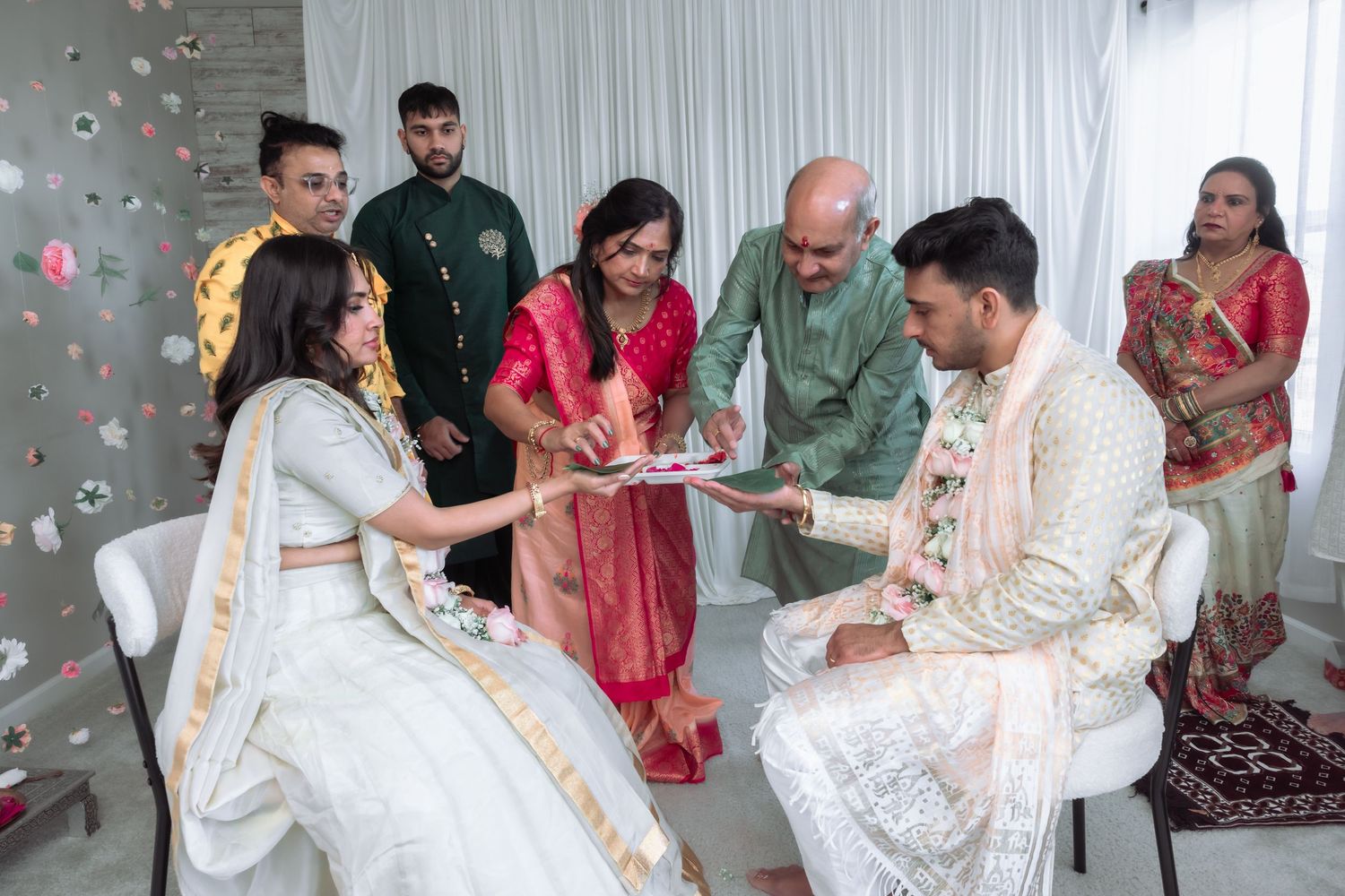 Family members present offerings to the bride and groom seated during a traditional Indian wedding ritual.